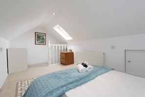 A bedroom with a skylight, a bed with a blue blanket, a wooden dresser, and a radiator. - Blue Becontree at Goresbrook London (Dagenham)