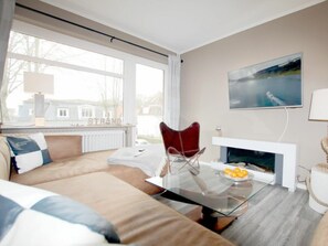 A modern living room with a glass coffee table, a red chair, a sofa, a fireplace, and a TV mounted on the wall. - E2 "nordmeer" at Feldstr. 18 (Wyk auf Foehr)
