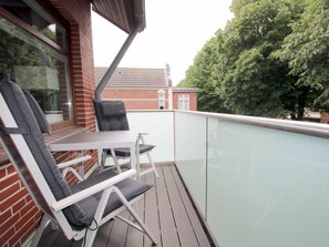 A balcony with a table and two chairs, a glass railing, and a view of trees and a building in the background. - E2 "nordmeer" at Feldstr. 18 (Wyk auf Foehr)