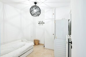 A small, white room with a bed, a hanging light fixture, a wall-mounted coat rack, and a door leading to a bathroom. - Renovated Apartment in Knokke-heist With Views (Knokke-Heist)