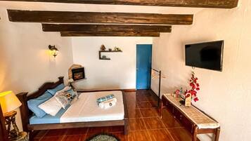 Un dormitorio con cama, mesita de noche, lámpara, televisor en la pared y una puerta azul.