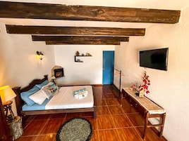 Un dormitorio con cama, mesita de noche, lámpara, televisor en la pared y una puerta azul.