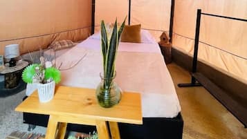 Habitación tipo tienda de campaña con una cama, una mesita pequeña y una planta en maceta.
