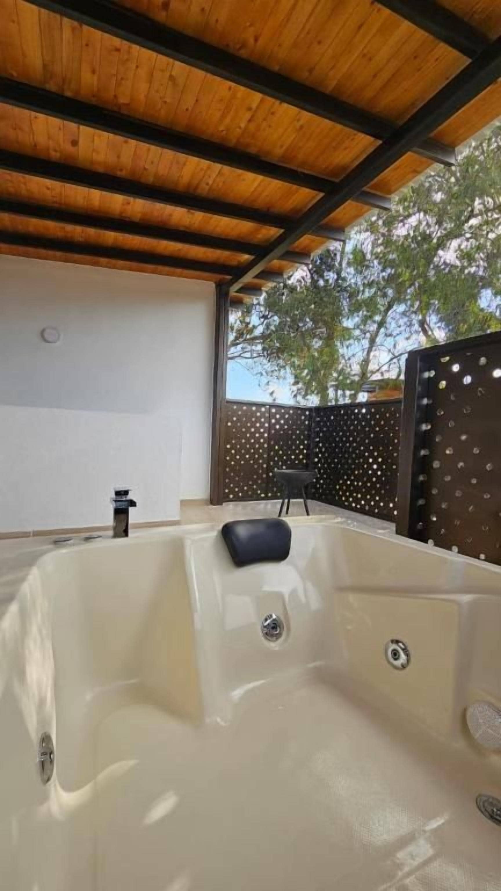 Un jacuzzi bajo un techo de madera, con un muro y una cerca al fondo.