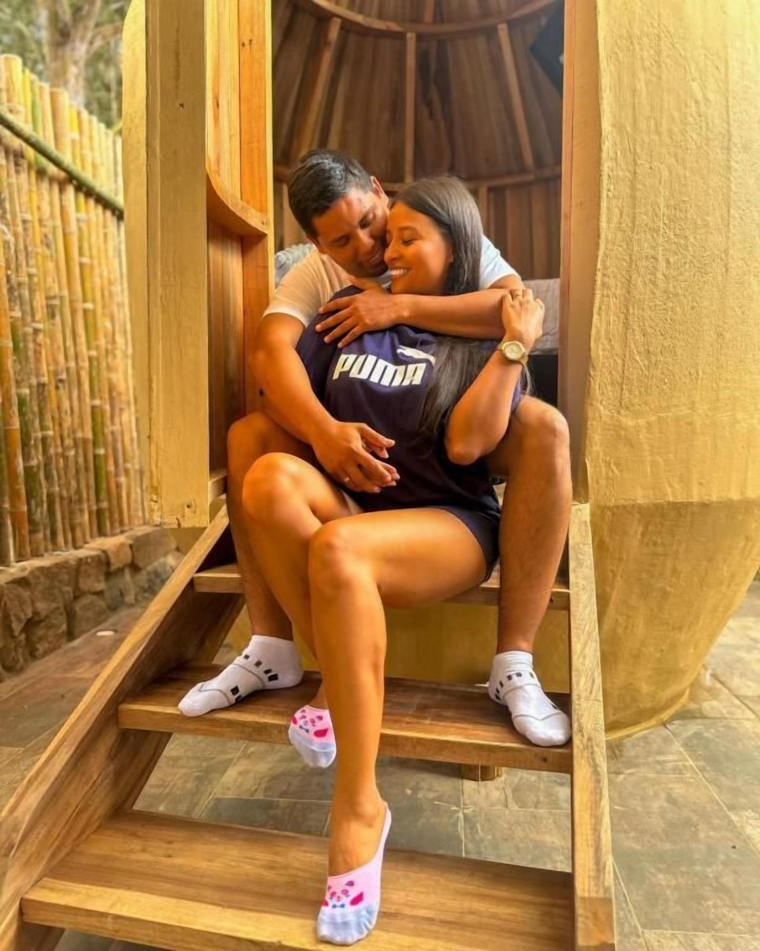 Una pareja sentada en escalones de madera con una valla de bambú al fondo.