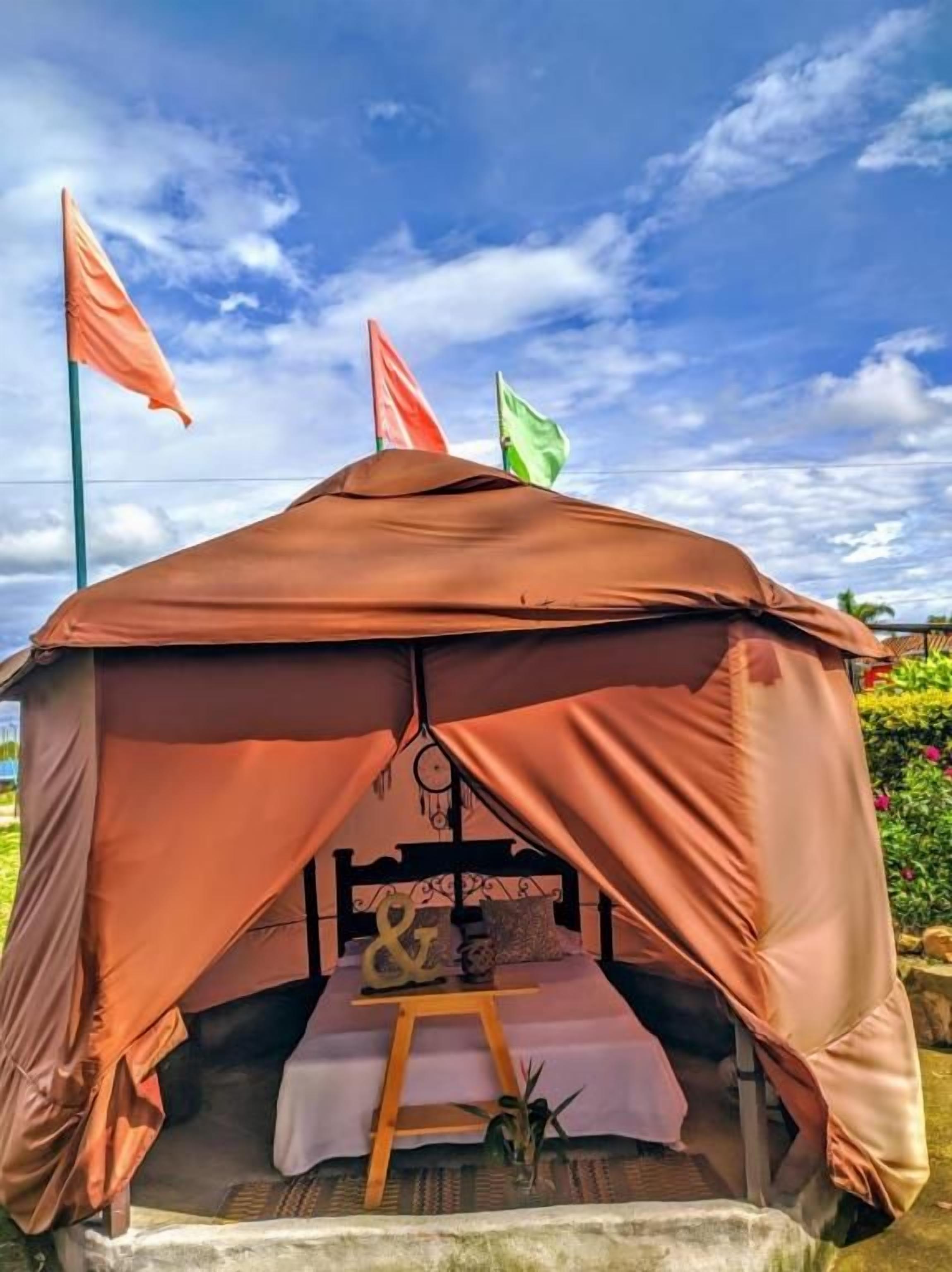 A tent with a bed, a table, and a hanging light fixture.