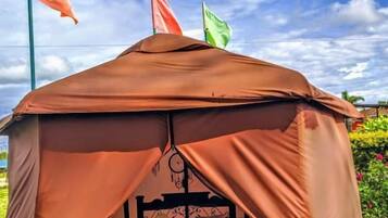 A tent with a bed, a table, and a hanging light fixture.