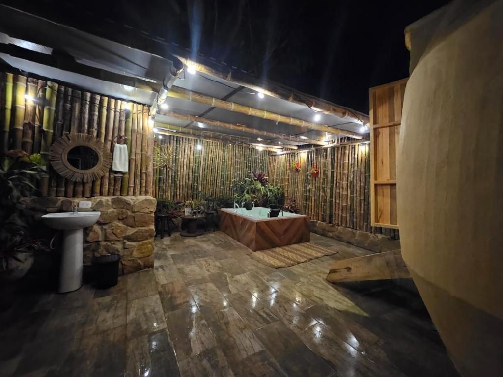 Un espacio al aire libre con un muro de piedra, un espejo redondo, una mesa con cubierta de vidrio y un barril de madera grande.