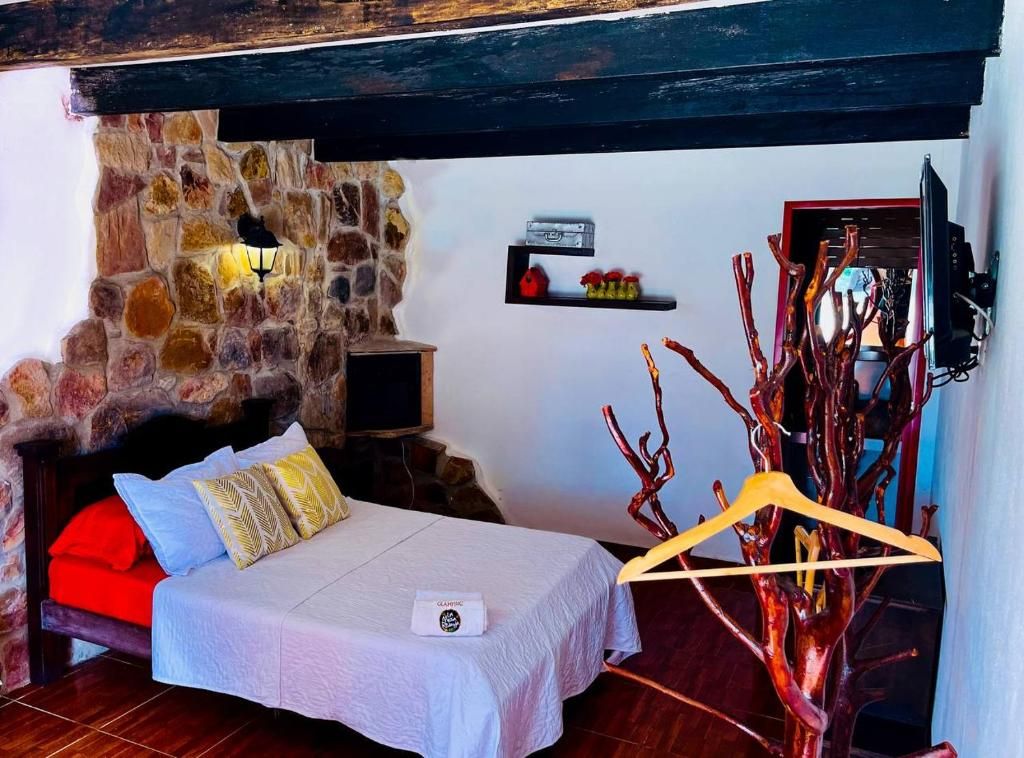 A bedroom with a stone wall, a bed with pillows, a TV, and a shelf with decorative items.