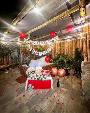 An outdoor dining area with a table set for a celebration, surrounded by bamboo walls and plants. - PARADOR LA MESA REDONDA (Los Santos)