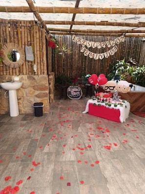Un entorno rústico al aire libre con un muro de piedra, un banco de madera y una mesa con mantel rojo.