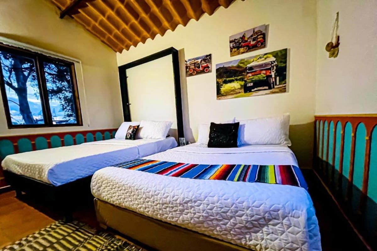 A room with two beds, a window with a view of trees, and wall art depicting vehicles.