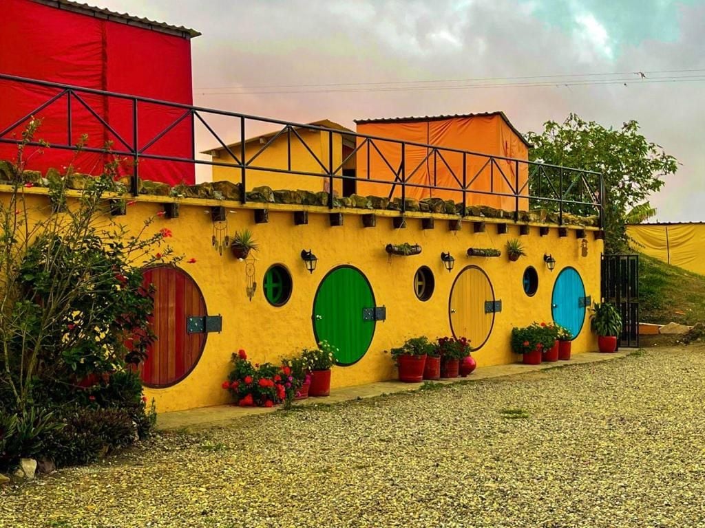 A building with multiple circular windows and doors, a red and yellow facade, and a gravel ground.