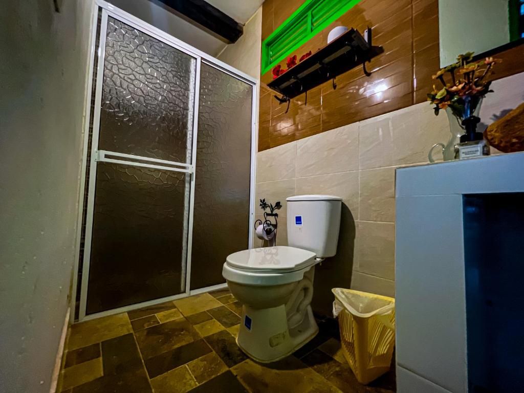 A bathroom with a toilet, a trash bin, a shelf with toiletries, and a decorative vase.