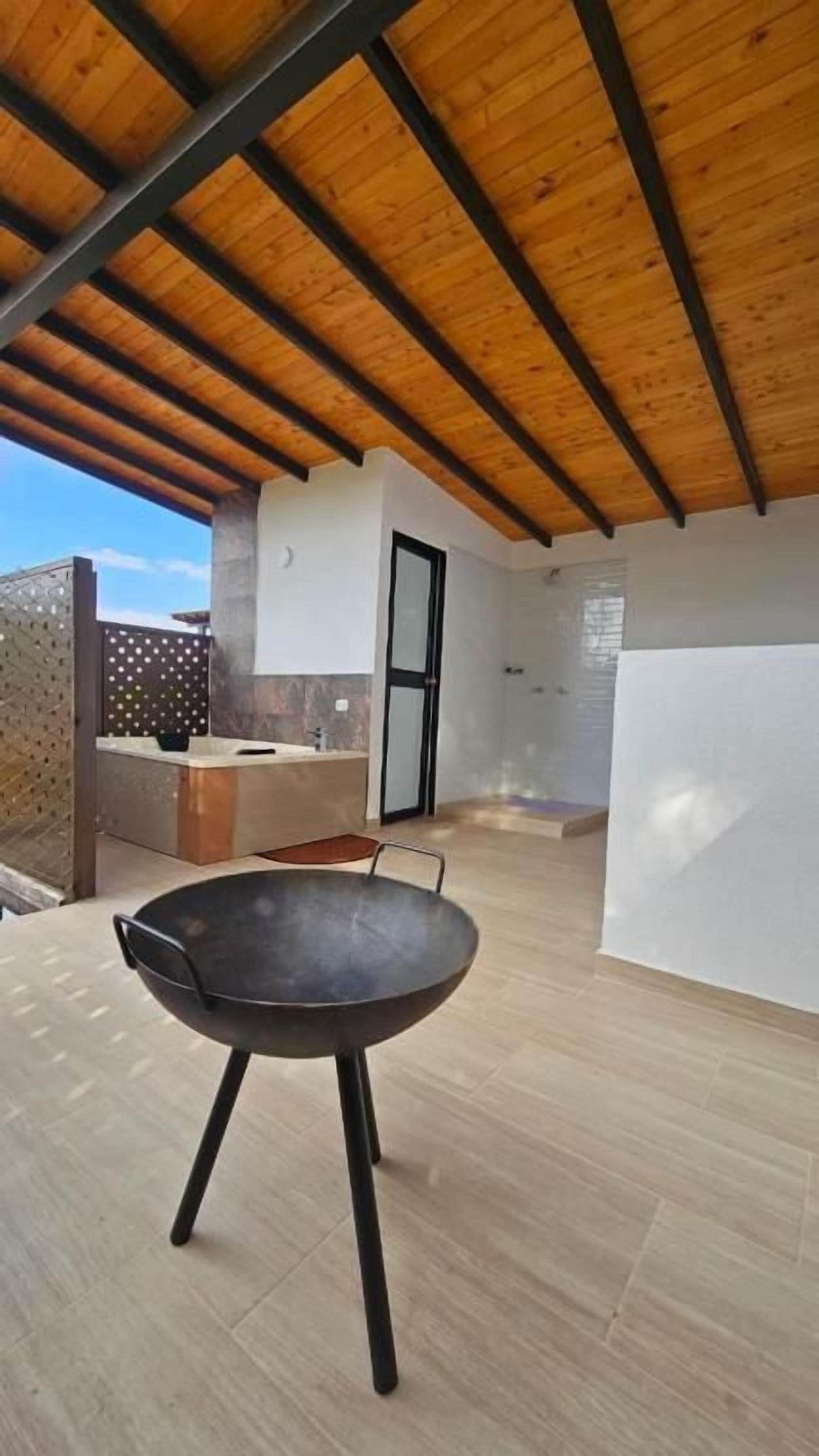 An outdoor patio with a round table and chairs, a wooden ceiling, and a white wall with a door.