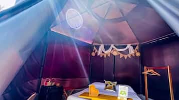 A tent with a bed, a small table, and a hanging light fixture.