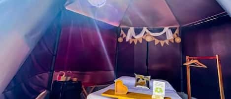 A tent with a bed, a small table, and a hanging light fixture.