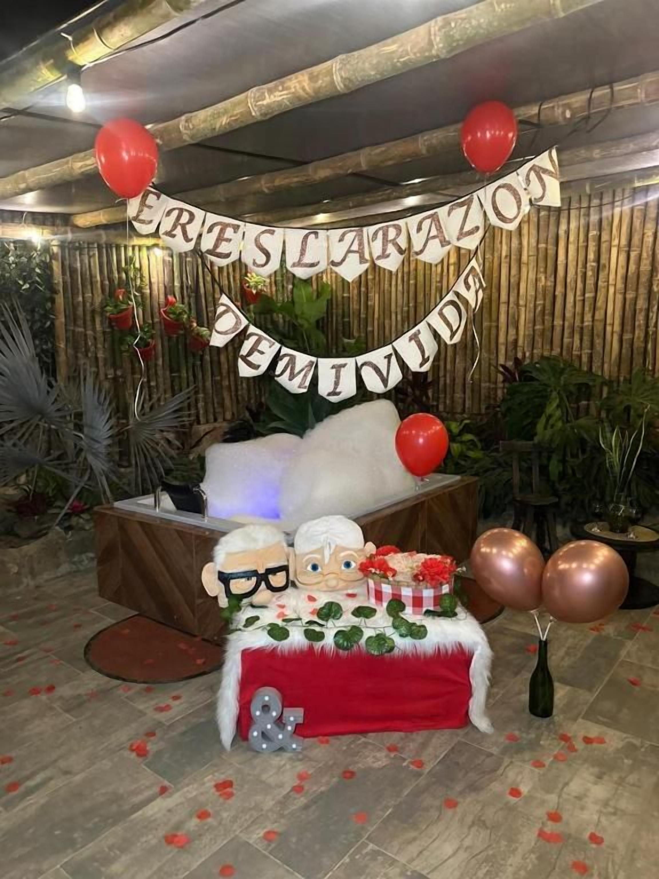 A decorated indoor space with a banner, balloons, and a table with a red tablecloth.