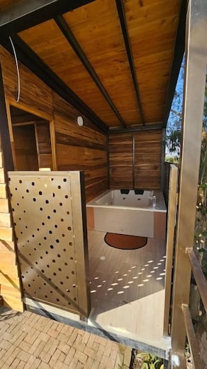 A wooden cabin with a metal door, a bathtub, and a brick floor. - PARADOR LA MESA REDONDA (Los Santos)