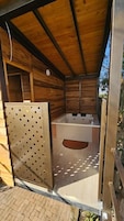 Una cabaña de madera con puerta metálica, bañera y suelo de ladrillo.