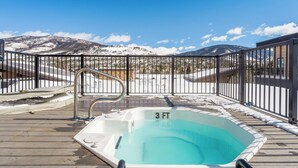 Un bain à remous de 90 cm de diamètre, installé sur une terrasse en bois, avec vue sur des montagnes enneigées.