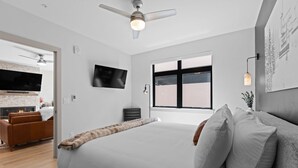 Une chambre moderne avec un grand lit, un téléviseur à écran plat, un ventilateur de plafond et une fenêtre donnant sur un beau paysage.