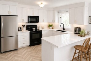 A modern kitchen with white cabinetry, stainless steel appliances, a herringbone floor pattern, and a central island with seating.