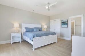 A bedroom with a white bed, two bedside tables with lamps, a ceiling fan, and a door with a painting. - Water views with pool and hot tub (North Topsail Beach)