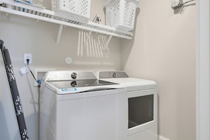 A front view of a white washing machine with a control panel, a power outlet, and a laundry basket on a shelf above. - Water views with pool and hot tub (North Topsail Beach)