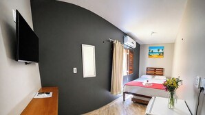 Et lille hotelværelse med seng, skrivebord, fjernsyn og aircondition.