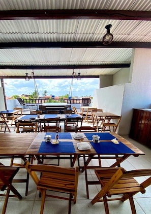 An outdoor dining area with wooden tables and chairs, a view of the cityscape, and a covered roof structure. - Vila Cactos Jeri (Jijoca de Jericoacoara)