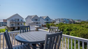 Une propriété située en bord de mer, dotée d’une terrasse avec une table ronde et des chaises, d’où l’on peut admirer une rangée de maisons avec des balcons.