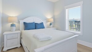 Une chambre à coucher avec un lit, deux tables de chevet avec des lampes, une fenêtre avec des stores et une vue sur les bâtiments à l’extérieur.