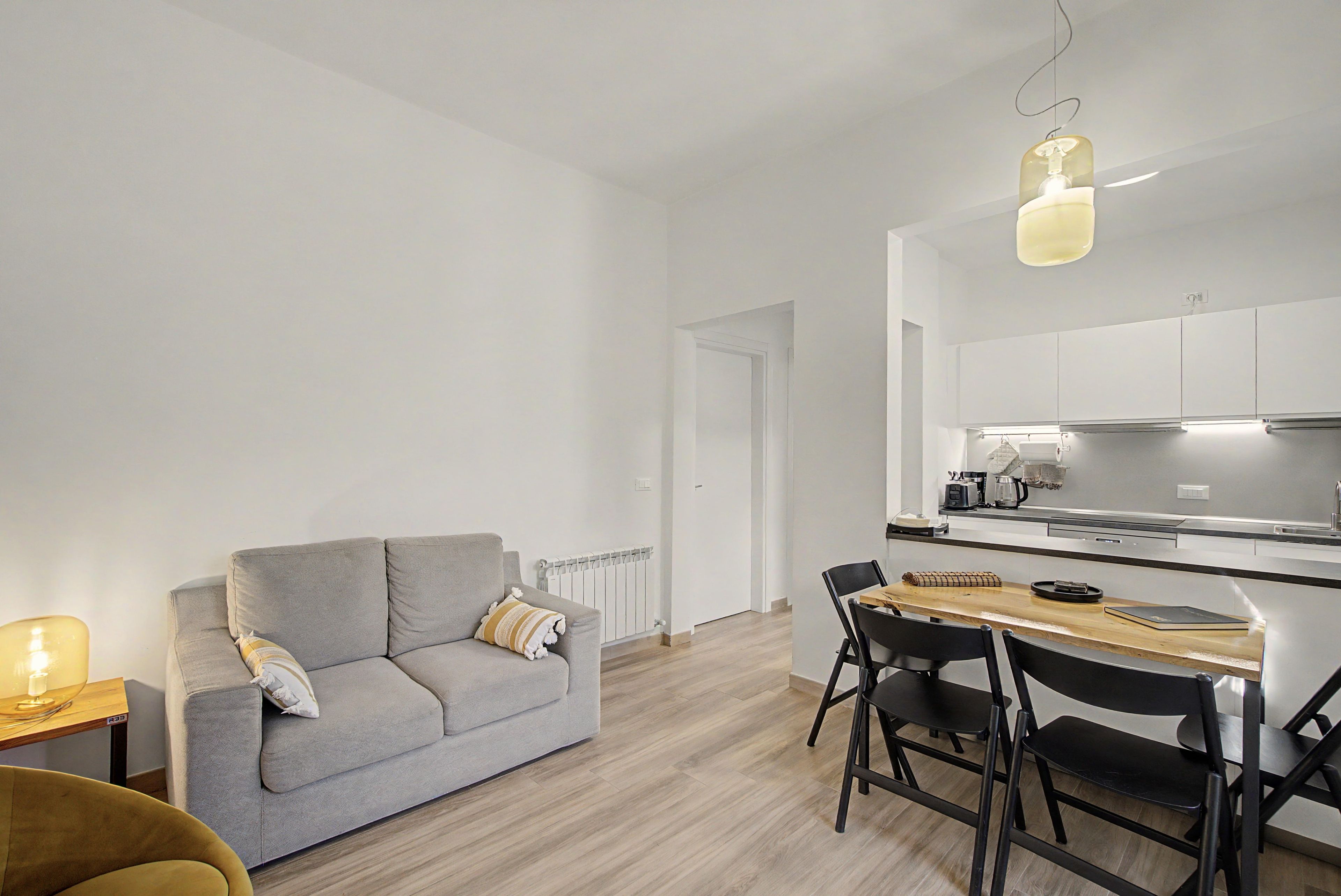 Eine moderne Küche mit weißen Schränken, einem Esstisch mit Stühlen und einem grauen Sofa inklusive Kissen.