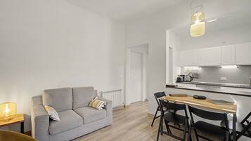 Eine moderne Küche mit weißen Schränken, einem Esstisch mit Stühlen und einem grauen Sofa inklusive Kissen.