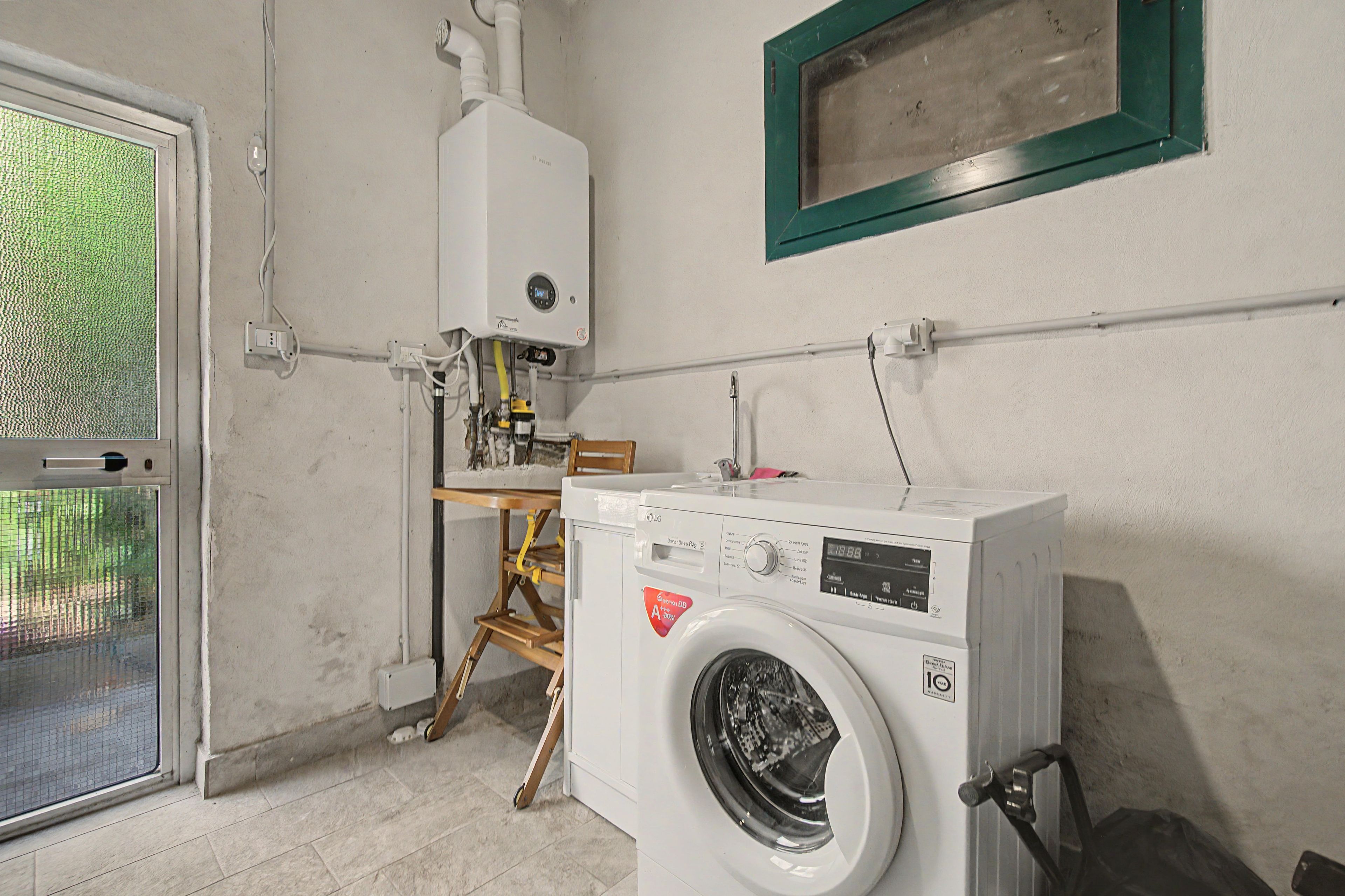 A laundry room with a washing machine, a heater, and a window with a green frame.