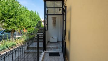 Ein schmaler Außenkorridor mit einem Metallzaun, einem Fliesenboden und einer weißen Bank.