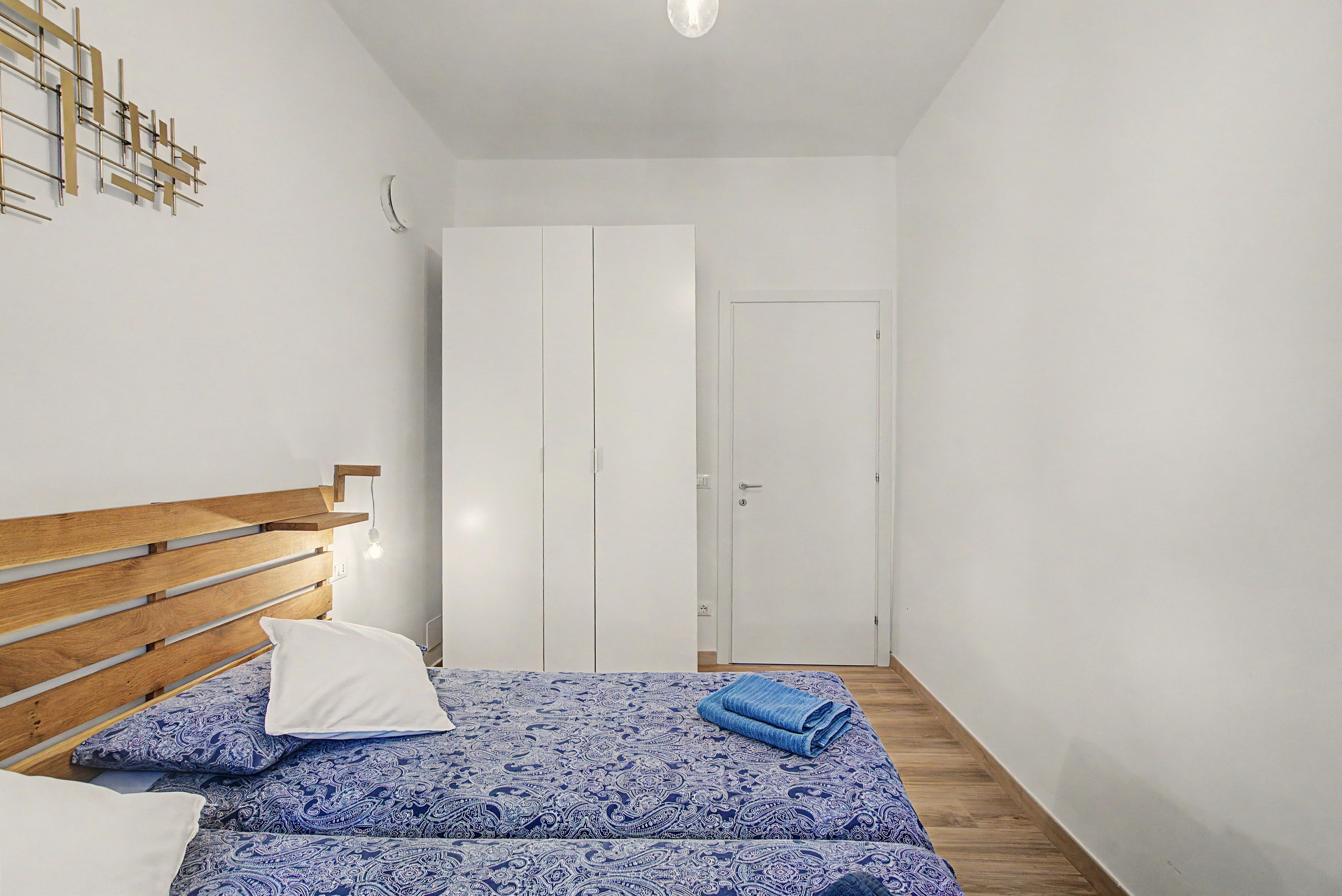A bedroom with a wooden bed, a white door, and a patterned bedspread.