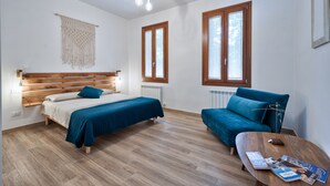 A modern bedroom with a wooden headboard, a bed with a blue bedspread, a blue sofa, a wooden coffee table with magazines, and a macramé wall hanging. - Holiday Home 'Il Melograno': Private Terrace, Private Parking, Wi-Fi, and Air Conditioning (Venezia)