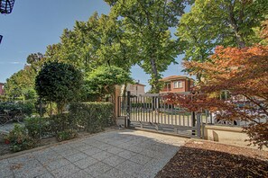 A paved courtyard with a metal gate, surrounded by trees and a building with a tiled roof. - Holiday Home 'Il Melograno': Private Terrace, Private Parking, Wi-Fi, and Air Conditioning (Venezia)