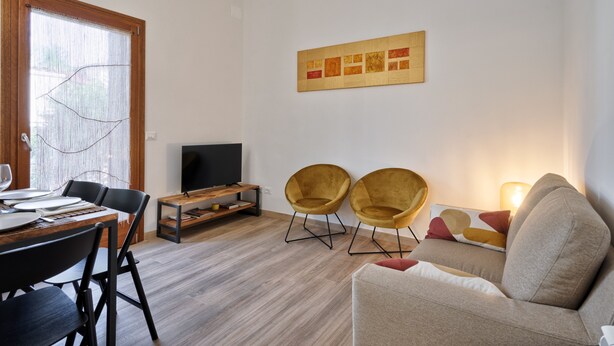 A modern living room with a wooden dining table, two armchairs, a sofa, a flat-screen TV, and a painting on the wall. - Holiday Home 'Il Melograno': Private Terrace, Private Parking, Wi-Fi, and Air Conditioning (Venezia)