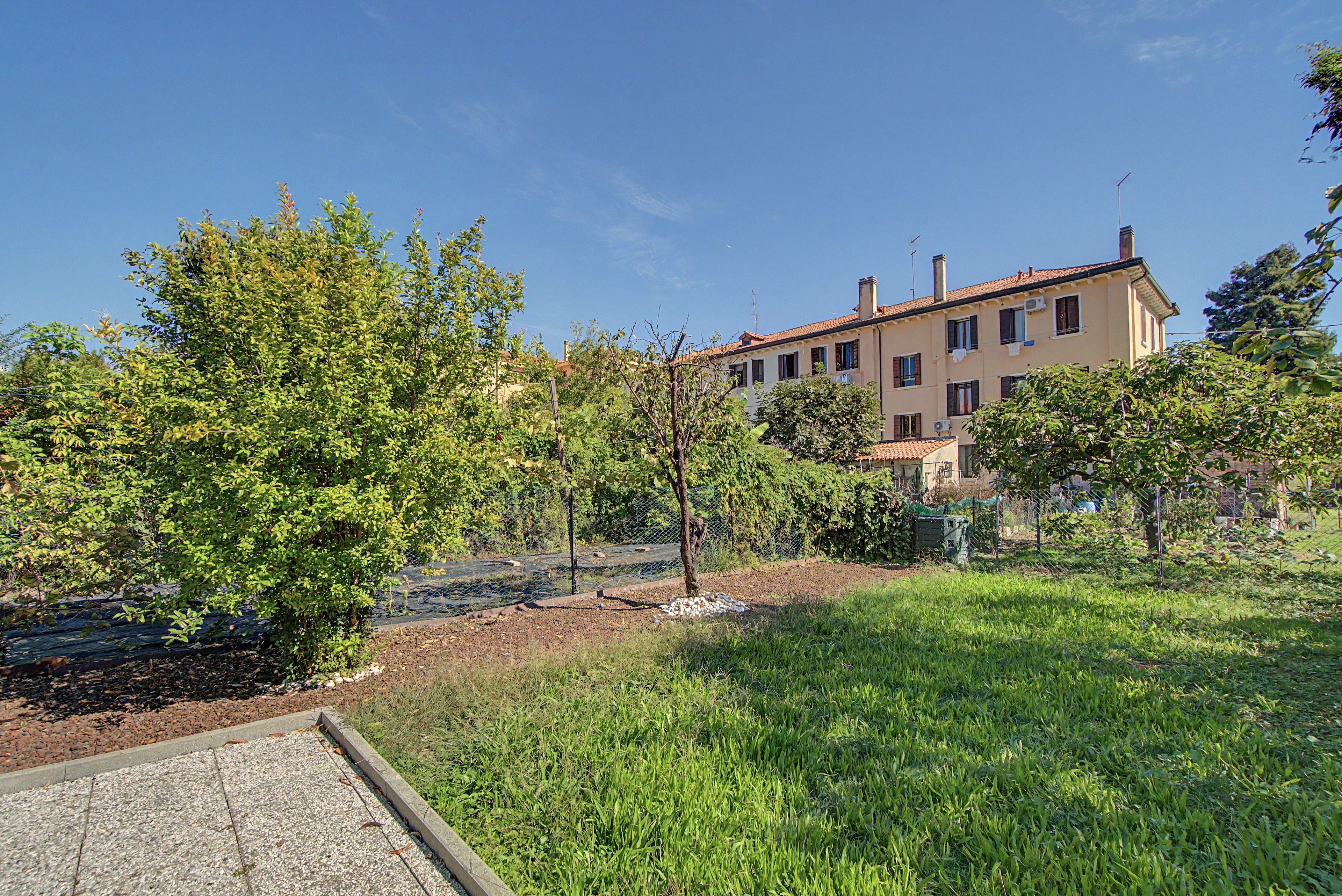 Edifício residencial com área de jardim, calçada pavimentada e cerca.