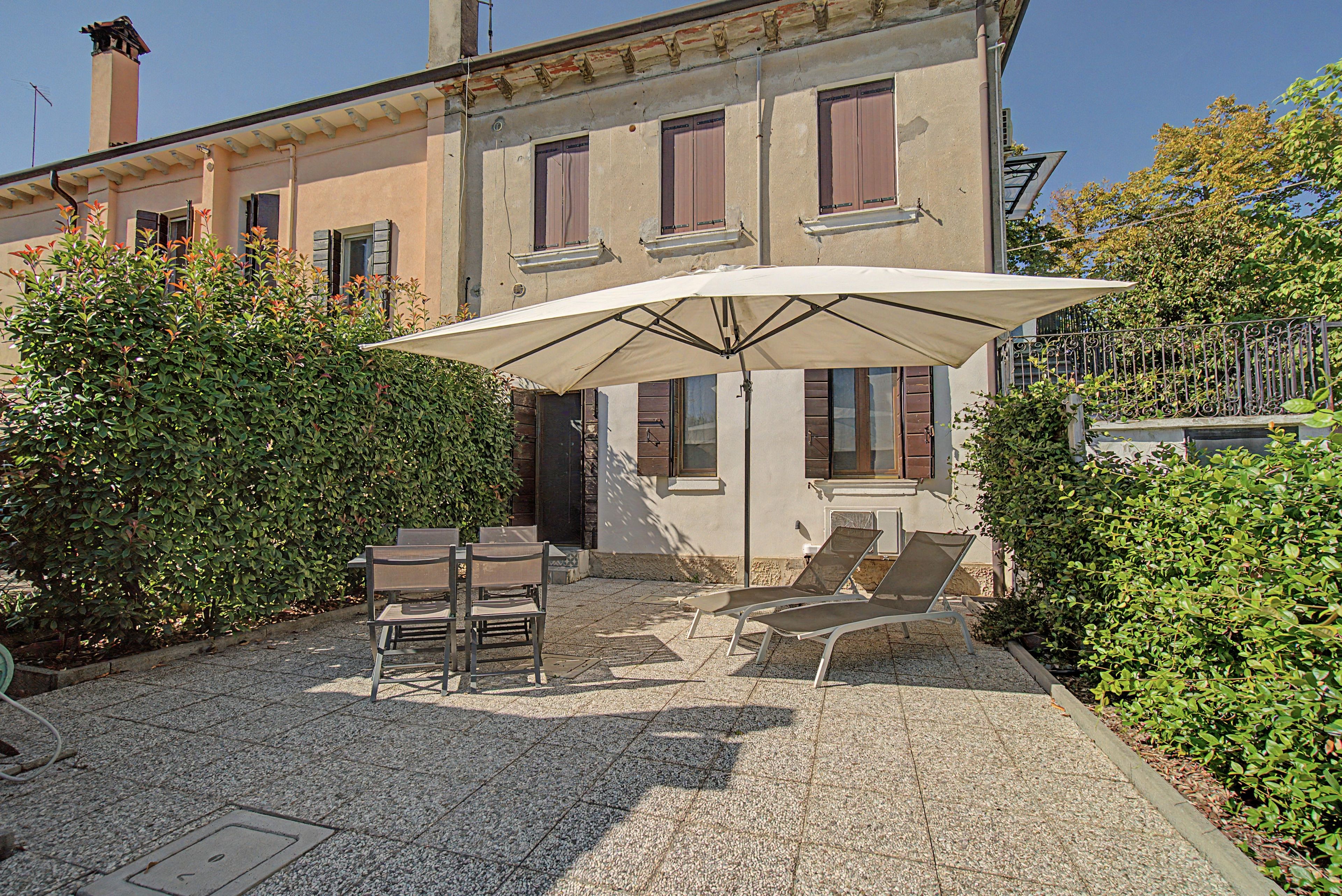 A patio with outdoor furniture, a large umbrella, and a building with multiple windows and shutters.
