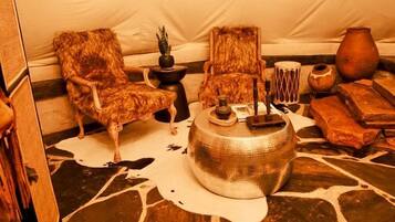 A tent interior with a stone floor, two chairs, a central table with a lamp, and various decorative items.