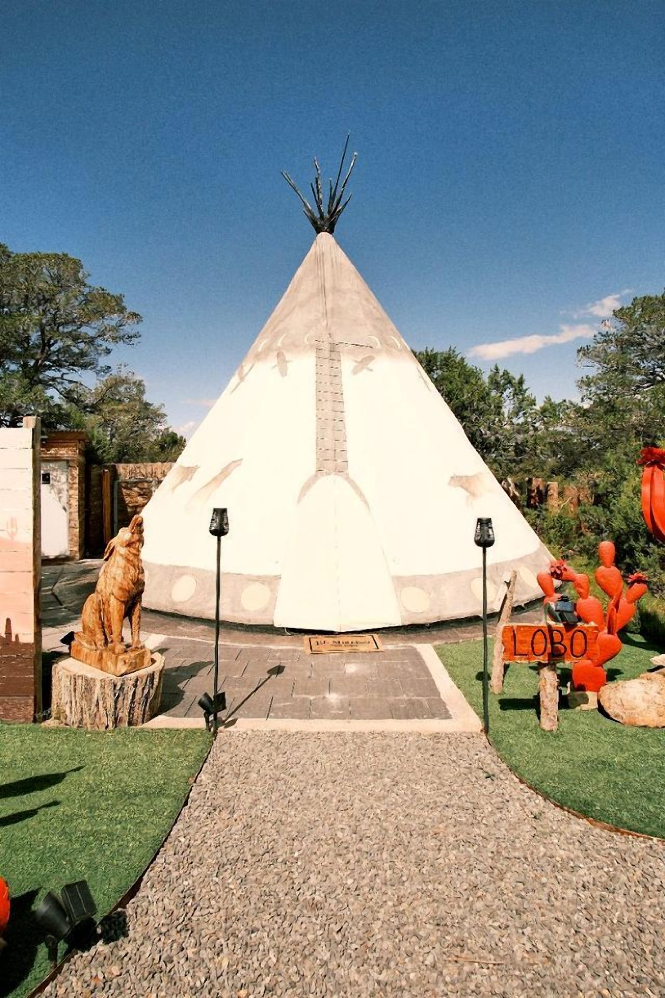 A tipi with a clear path leading to it, surrounded by a landscaped area with a statue and a sign.