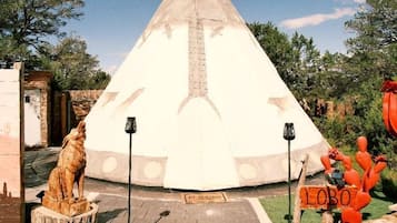 A tipi with a clear path leading to it, surrounded by a landscaped area with a statue and a sign.