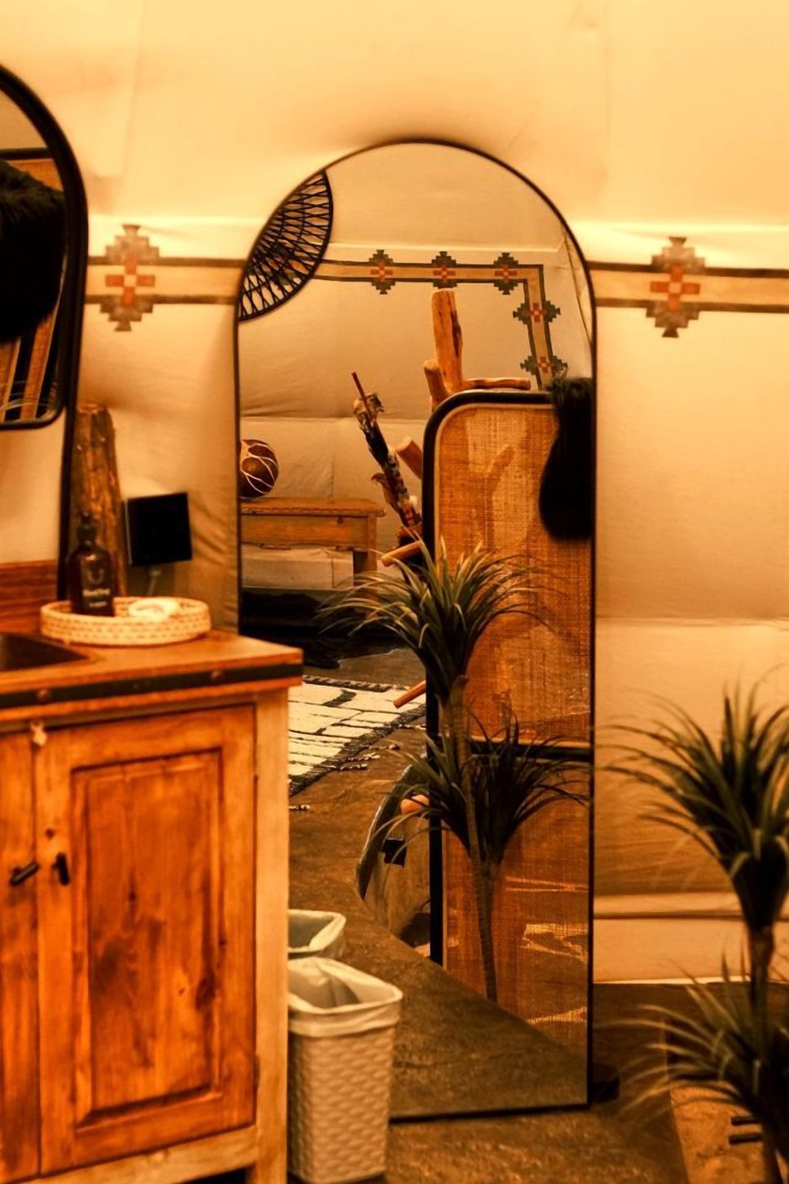 Una habitación con un armario de madera, un espejo que refleja una cama, una guitarra y una planta.