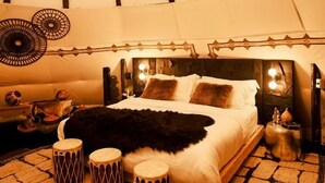 Une chambre confortable aménagée comme une tente, avec un lit, des oreillers, un plaid en fausse fourrure et un tapis à motifs.