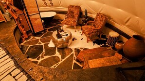 Un coin salon accueillant avec un sol en pierre, une table basse ronde, deux fauteuils confortables, une petite table agrémentée d’un objet décoratif et un grand vase.