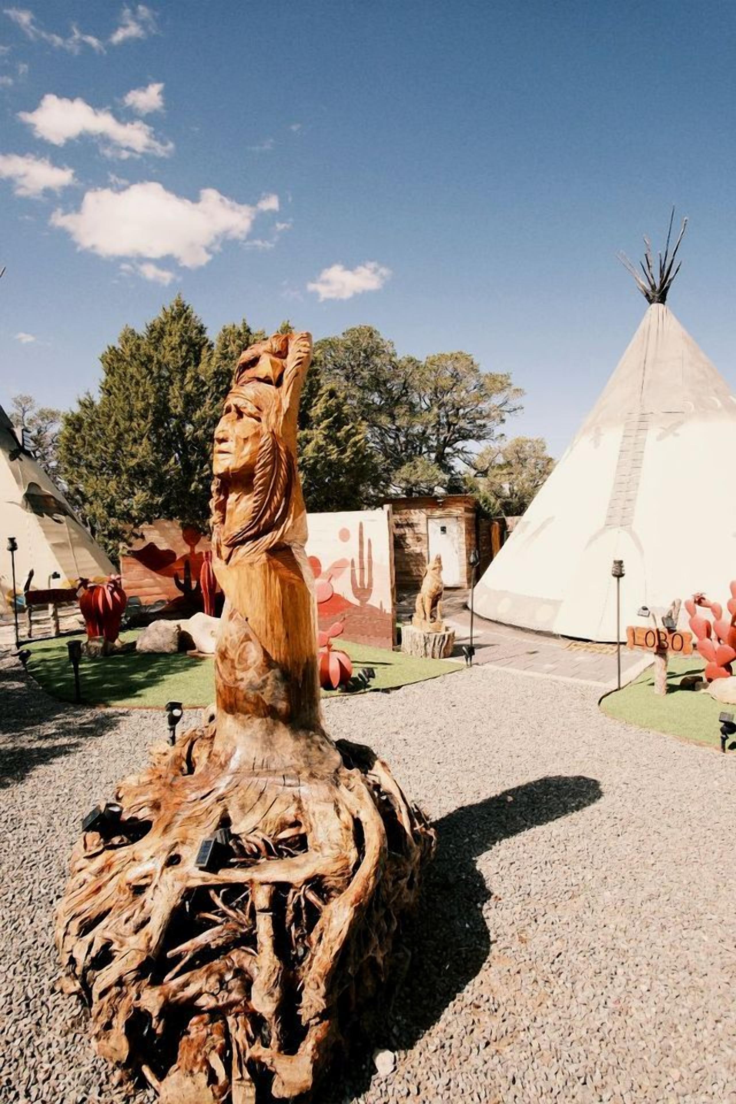 En träskulptur med en utskuren figur, ett tipi-tält och en skylt med ordet ”LOBO”.